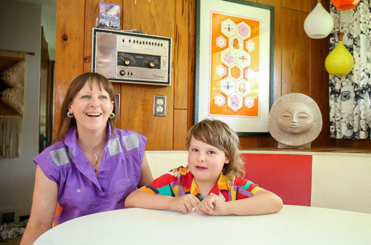  Kelly Elliott and her son Mickey share a laugh in the original mid-century modern kitchen, which boasts pops of orange, red and yellow. Elliott shared that the kitchen is where the whole family gathers and that she still uses the original stove from the 1960s that came with the home.  