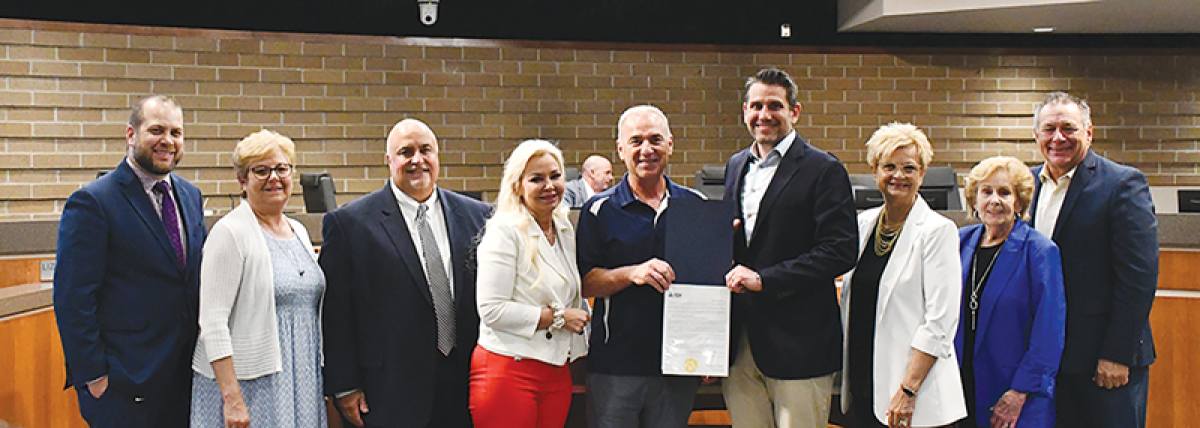  Michael Sekich, center, wearing a navy blue and white shirt, holds up a resolution alongside Sterling Heights City Council members and Stevenson High School Principal Kenneth Cucchi III June 4. The council honored Sekich’s 34-year career in music education due to Sekich’s retirement from his role as Stevenson’s director of instrumental music. 