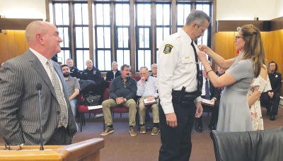  As Grosse Pointe Farms Public Safety Director John Hutchins, at left, looks on, new Farms Lt. Frank Zielinski has  his badge pinned onto his  uniform by his wife, Rita. 