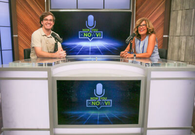     Trevor Walega, a Novi video production specialist, and Sheryl Walsh-Molloy, Novi communications director, sit in front of a video wall set up for one of the city's podcasts. 