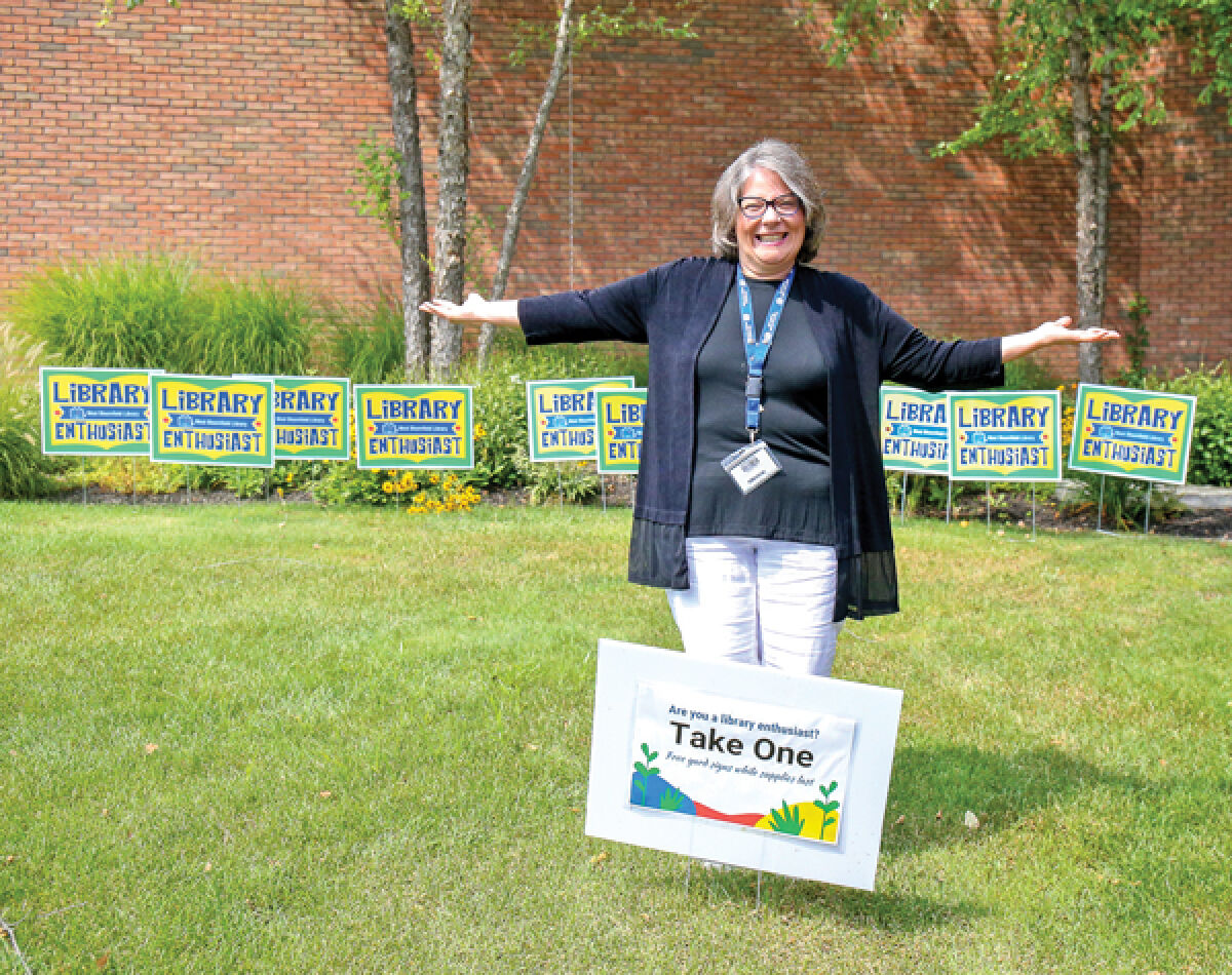  The West Bloomfield Township Public Library has elected to have a millage proposal placed on ballots in November. The library’s director, Cathy Russ, is pictured with “library enthusiast” yard signs that have been offered to patrons. 