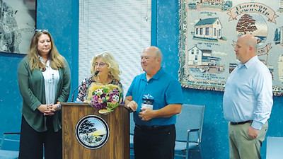  Sue and James Keehn (center left and right) stand at the podium after being named Harrison Township’s 2024 Hometown Heroes.  