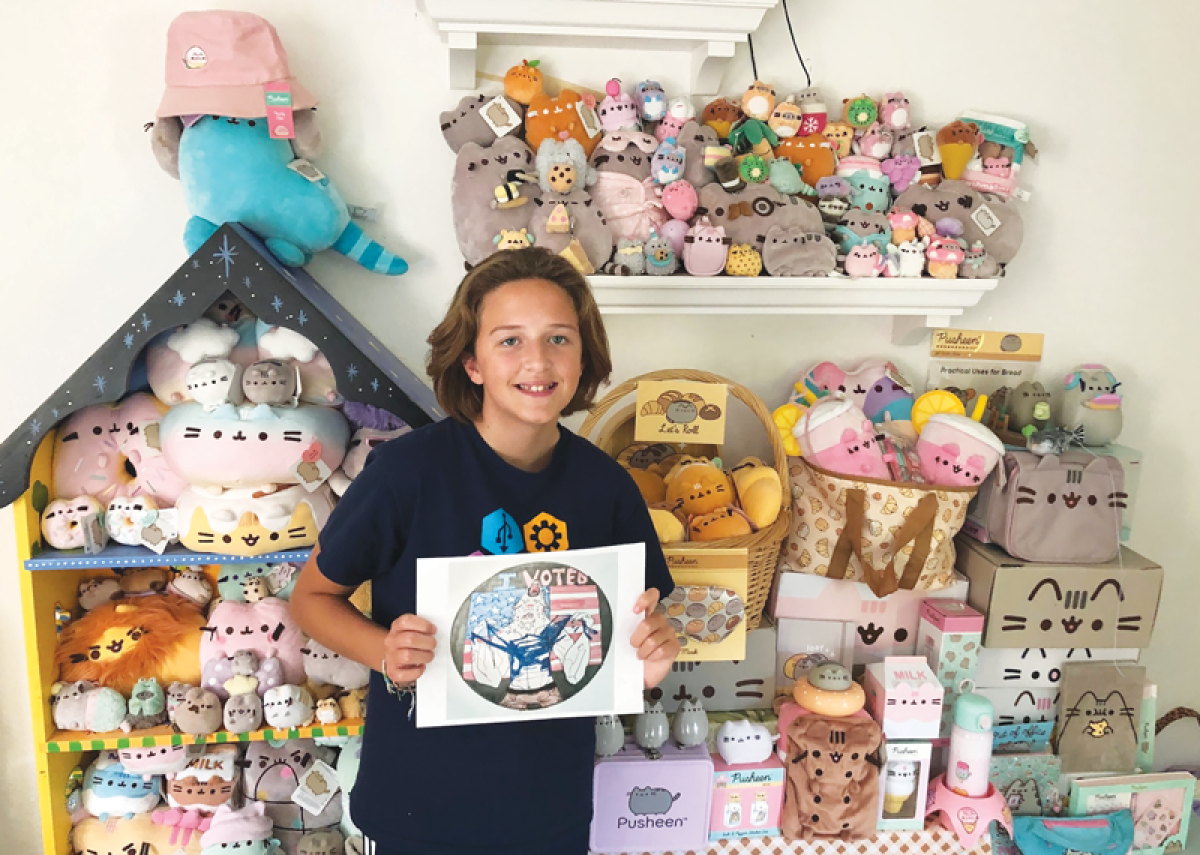  Brownell Middle School student Jane Hynous holds her winning “I Voted” sticker design as she stands in front of her collection of Pusheen memorabilia. 