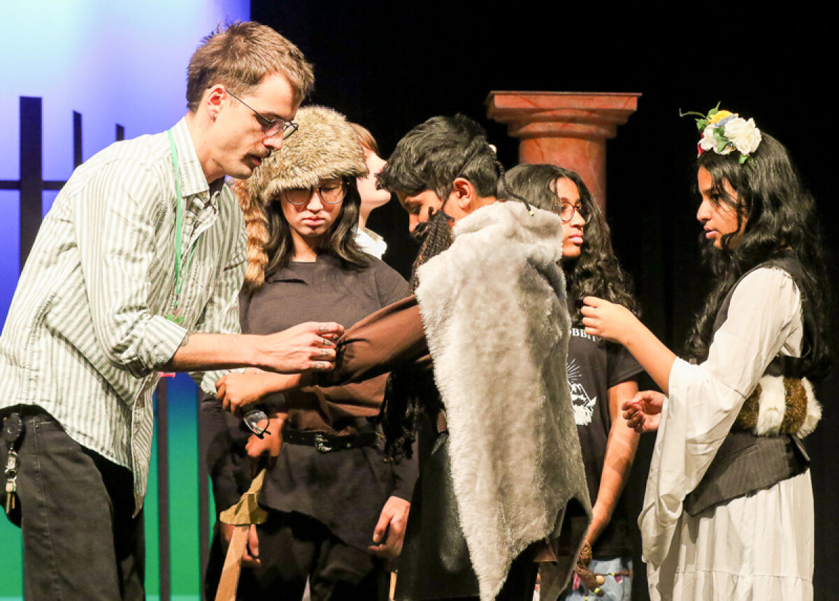  Novi Middle School theater director Joseph Green helps Aarav Chakravartti with his costume, as other students watch, during a dress rehearsal of “The Hobbit” Oct. 12. 