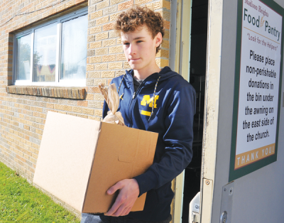  Nolan Knapp, a senior at Lamphere High School and a member of the National Honor Society, volunteers with the pantry. He is seen here carrying a box of groceries to a recipient’s car. 