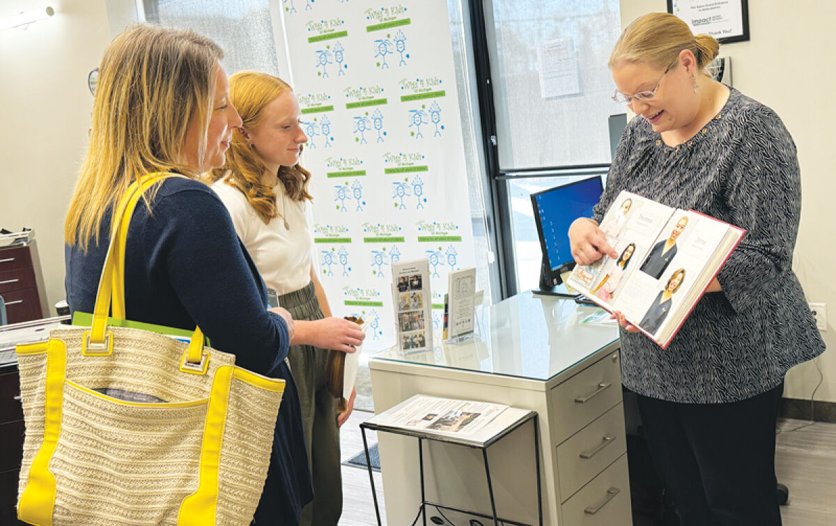  Jennifer Fisher, Maggie’s Wigs 4 Kids of Michigan development director, shows Jillian and her mom Amanda a book with pictures of children who received wigs from the organization. 