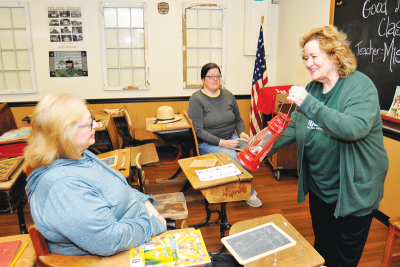  Margene Scott, right, chair of the Madison Heights Historical Commission, takes the teacher role inside a replica of a one-room schoolhouse at the Heritage Rooms at Madison Heights City Hall. Joining her are co-chair Jennifer Ballantine, in the background, and Debbie Boucher.  