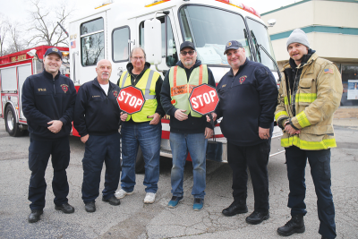   Utica Firefighter/paramedic Mike Ryan,  firefighter/EMT Mark Ricketts, crossing guard Mike Delicata, crossing guard Scott Milne, firefighter/EMT Andrew Doroh and firefighter/paramedic Yarema Petrusha pose with the two LED stop signs that the Utica Firefighters Association and Foundation bought for Hahn Street’s intersections with Cass Avenue and Van Dyke Avenue. 