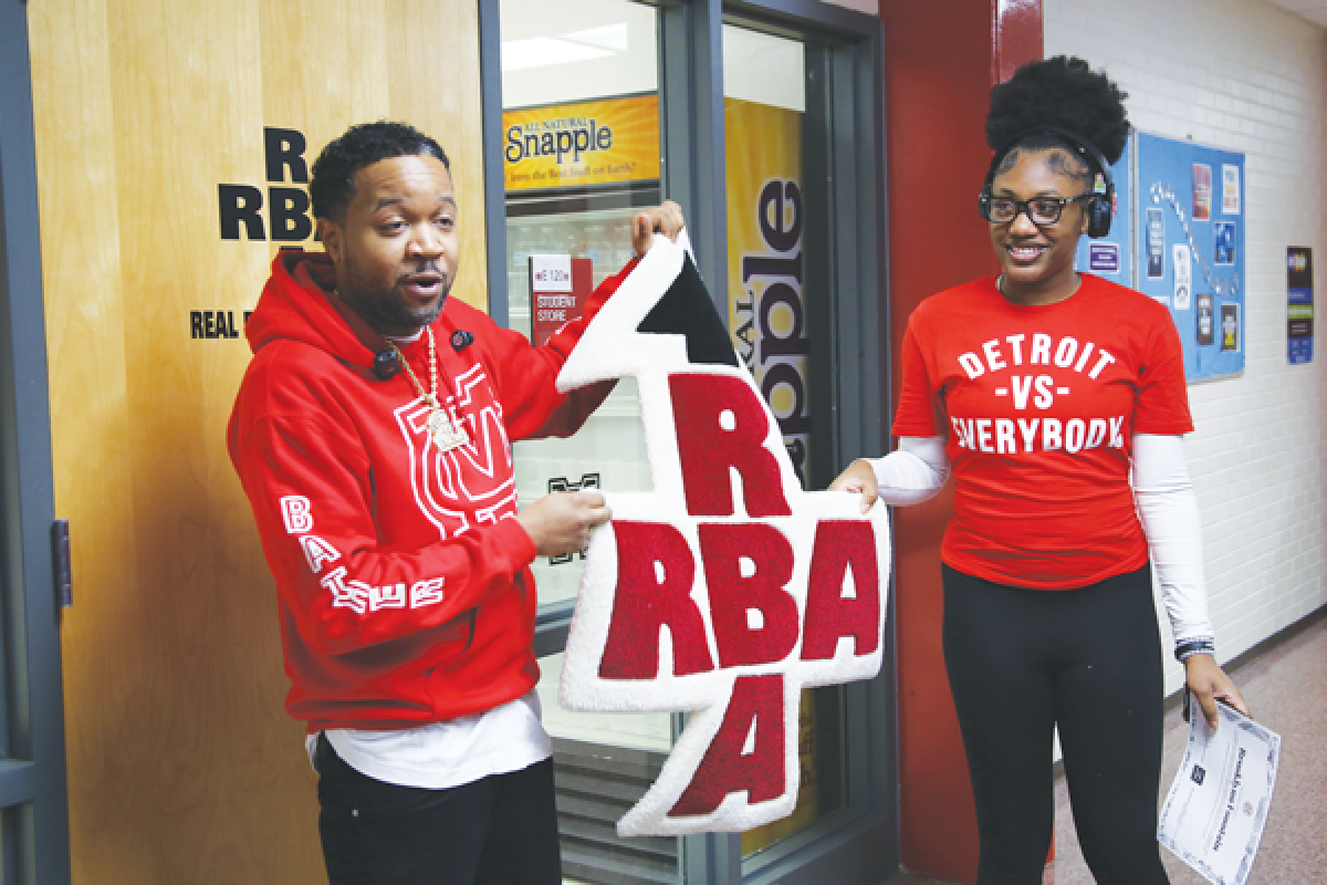  Tommey Walker, founder of Detroit VS Everybody, and Brooklyn Fountain, a 17-year-old Mount Clemens High School senior, hold up a rug in the shape of the school store’s new logo that Fountain designed as part of a Fashion Entrepreneurship course led by Walker. Fountain and Walker are wearing each other’s creations. Fountain is wearing a Detroit VS Everybody shirt while Walker’s sweatshirt features Fountain’s other design created through the class, “Bather Flavor.” 